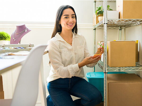 Woman smiling while putting a sticky note on a box that is on a silver shelf