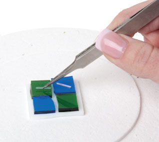 tweezers placing a glass rod on a green glass square